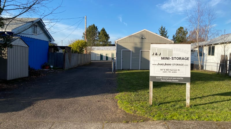 Front sign and entrance to J & J Mini-Storage at 507 Harrison St in Lebanon, OR next to blue house